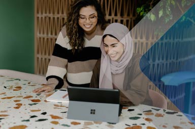 Two women smiling at a computer to illustrate how to pay international employees