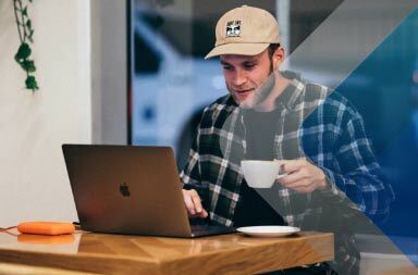 Man drinking at table while on laptop to illustrate article on hiring remote workers in other countries. By Kal Visuals on Unsplash.