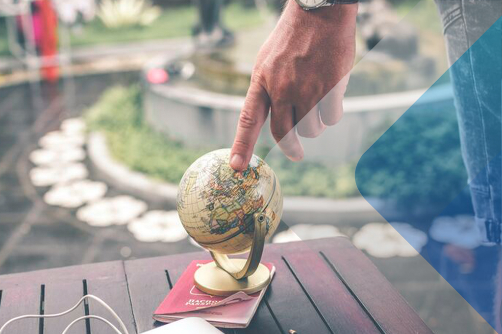Person pointing at globe to illustrate article on hiring contractors overseas. By Artem Beliaikin on Unsplash.